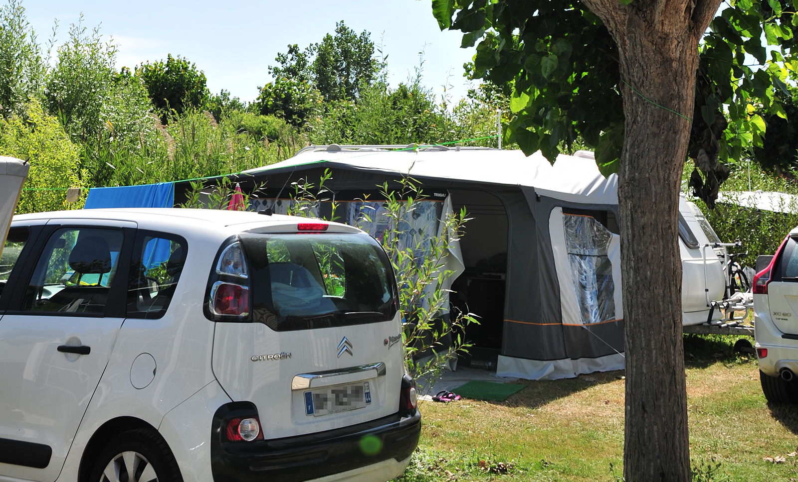 White car parked in front of a tent under the trees of La Prairie campsite in Saint-Hilaire