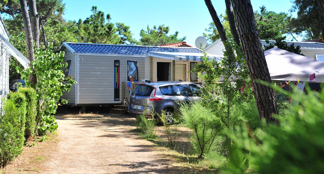 Mobile home in the shade of tall trees at Le Clos des Pins campsite in Vendée