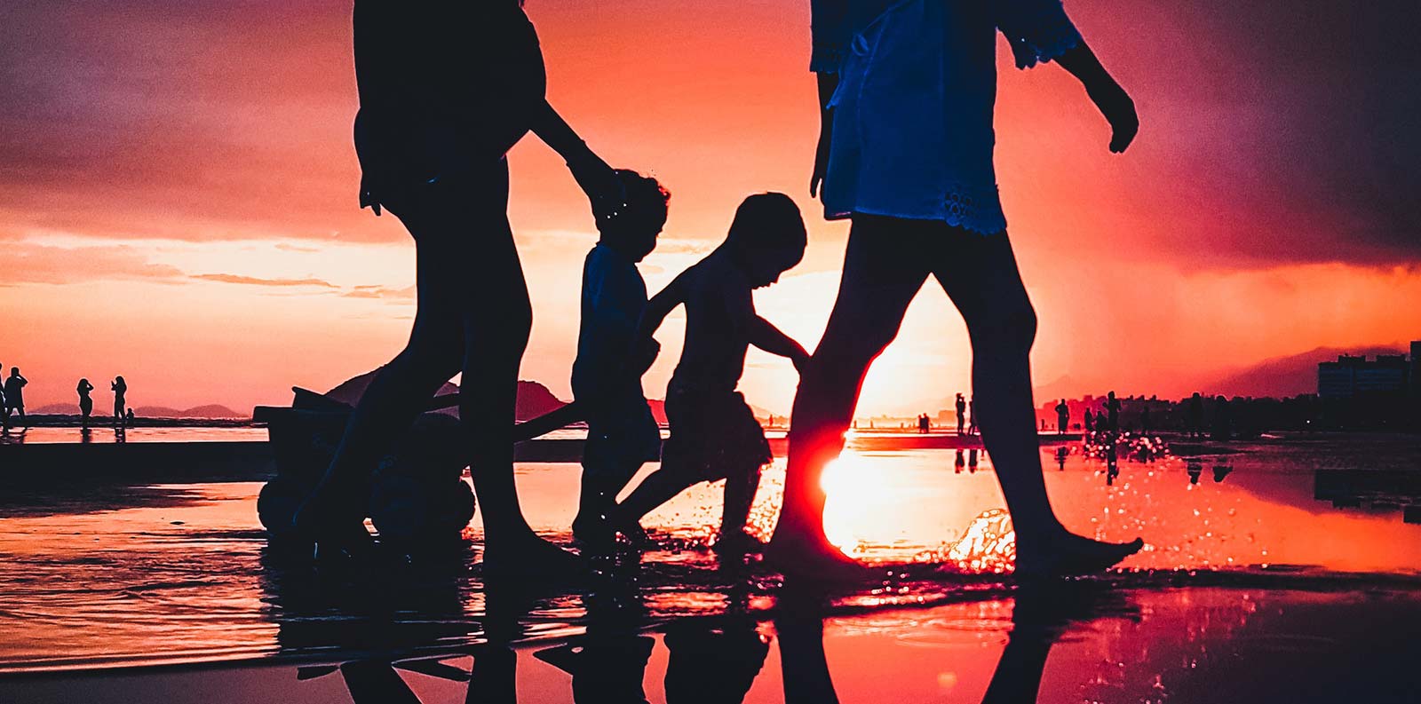 Familie van kampeerders die bij zonsondergang op het strand van Saint-Hilaire lopen