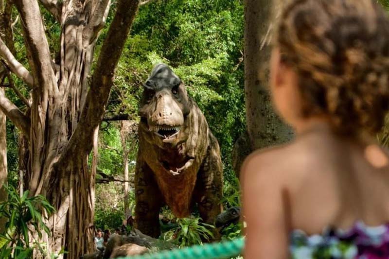 Klein meisje voor een standbeeld van een tyranosaurus in Dinos Park in de Vendée