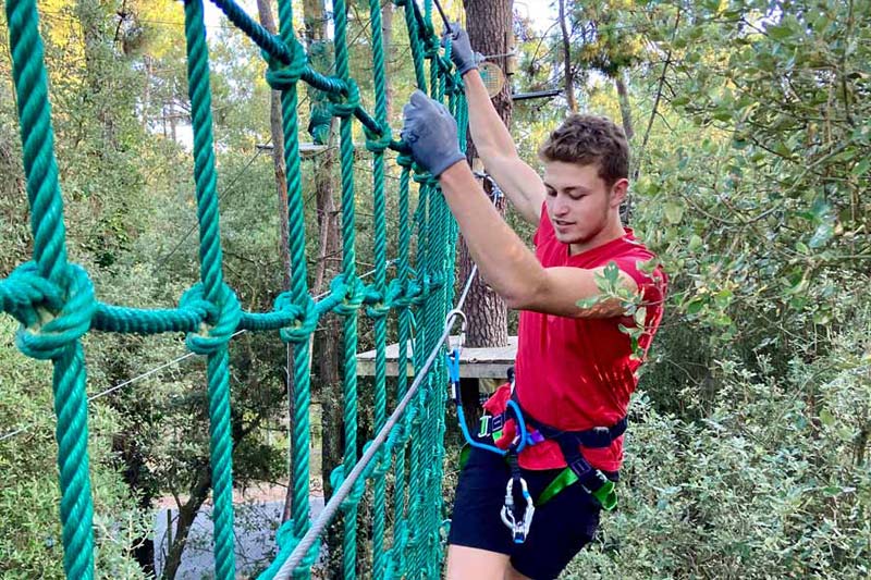 Young man climbing a rope wall in a park near the campsite