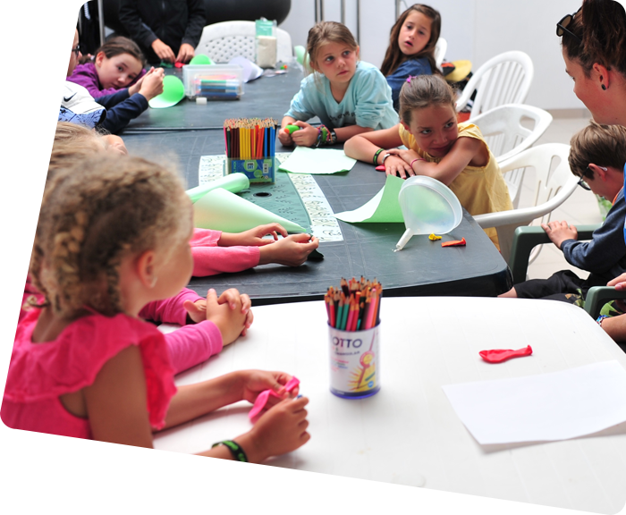 Enfants assis devant des tables avec crayons de couleur au club-enfants du camping à Saint-Hilaire