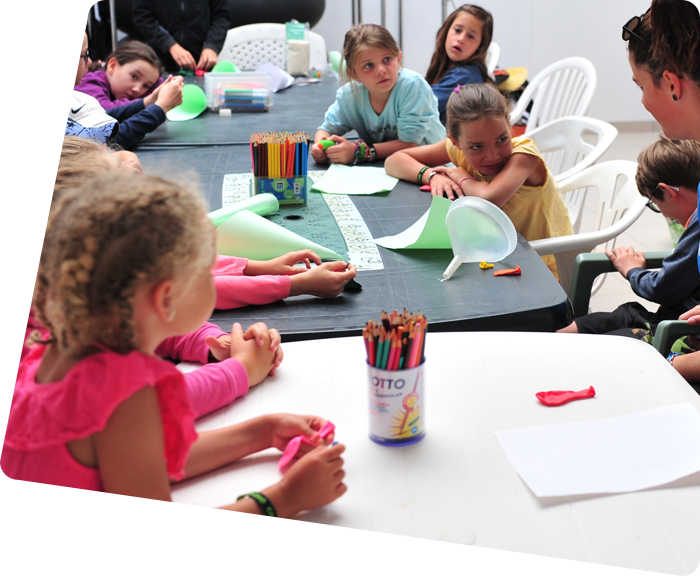 Children sitting in front of tables with colored pencils at the children's club of the campsite in Saint-Hilaire