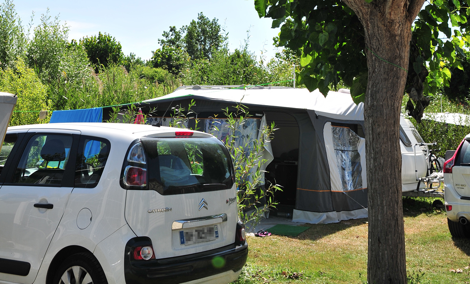 Witte auto geparkeerd voor een tent onder de bomen van camping La Prairie in Saint-Hilaire