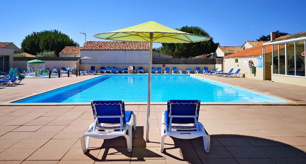 Transats sous un parasol jaune devant la piscine du camping la Prairie à Saint-Hilaire