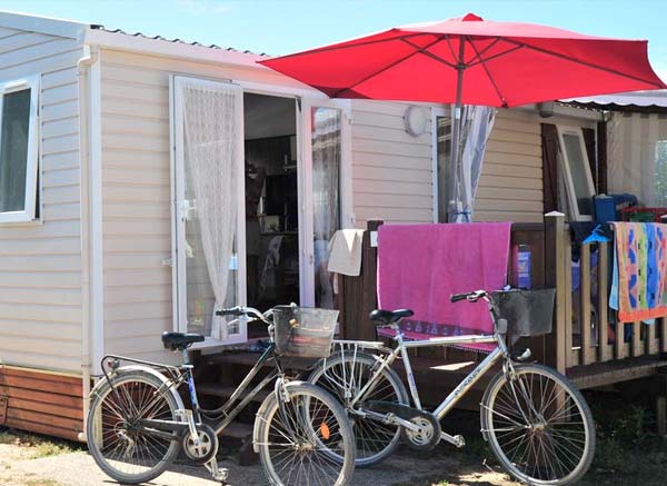 Vélos devant un mobil-home à louer et parasol rouge au camping à Saint-Hilaire en Vendée