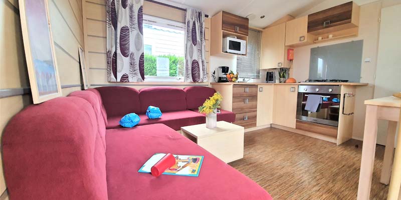 Living room with sofas and kitchen area in a mobile home for rent in Vendée